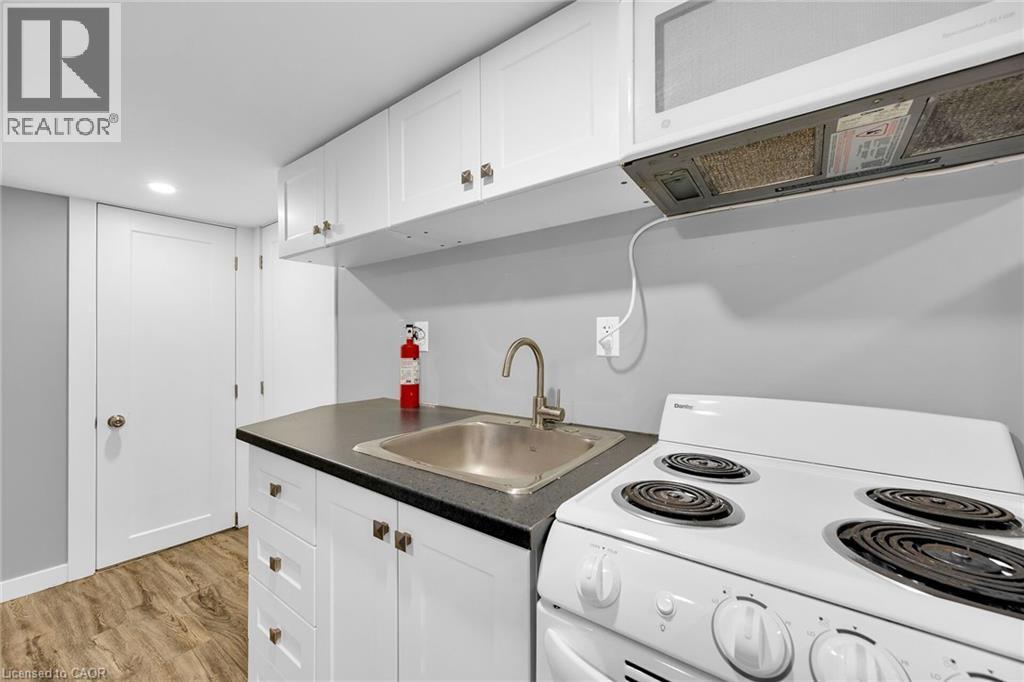 Kitchen with white electric range oven, a sink, dark countertops, white cabinets, and light wood-type flooring - 129 Dundurn Street N, Hamilton, ON - Indoor Photo Showing Kitchen