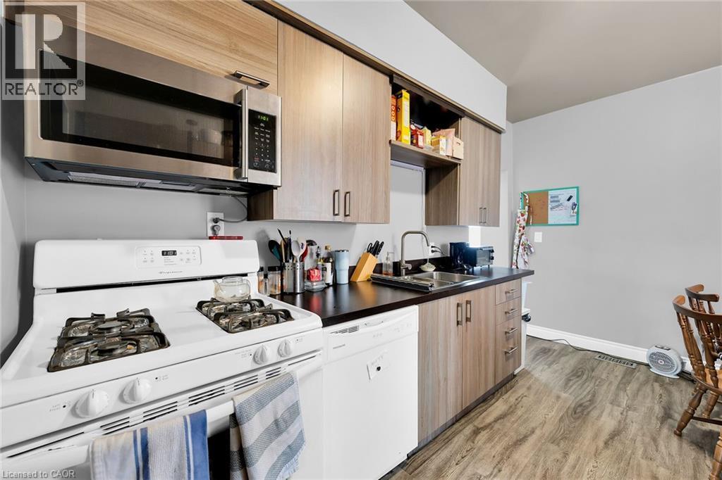 Kitchen with white appliances, a sink, light wood-style floors, dark countertops, and open shelves - 129 Dundurn Street N, Hamilton, ON - Indoor Photo Showing Kitchen With Double Sink