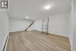 Finished basement with baseboard heating, stairway, and light wood finished floors -