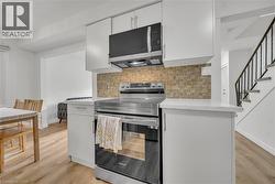 Kitchen featuring stainless steel appliances, backsplash, white cabinetry, light stone counters, and light wood-style flooring -