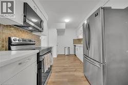 Kitchen featuring stainless steel appliances, white cabinets, tasteful backsplash, light wood-style flooring, and light stone countertops -