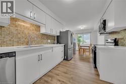Kitchen featuring decorative backsplash, appliances with stainless steel finishes, white cabinets, and light wood-style floors -