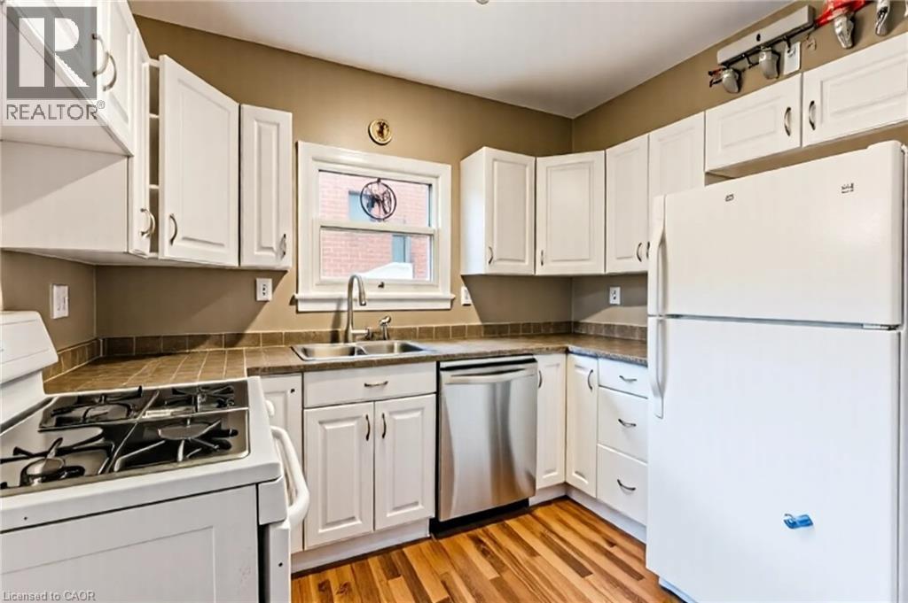 Kitchen featuring white appliances, white cabinets, and light wood-style floors - 172 Markland Street, Hamilton, ON - Indoor Photo Showing Kitchen With Double Sink