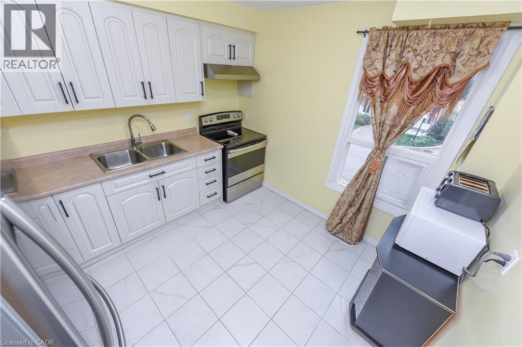Kitchen featuring stainless steel appliances, white cabinets, light countertops, under cabinet range hood, and light tile patterned flooring - 85 Enmount Drive, Brampton, ON - Indoor Photo Showing Kitchen With Double Sink
