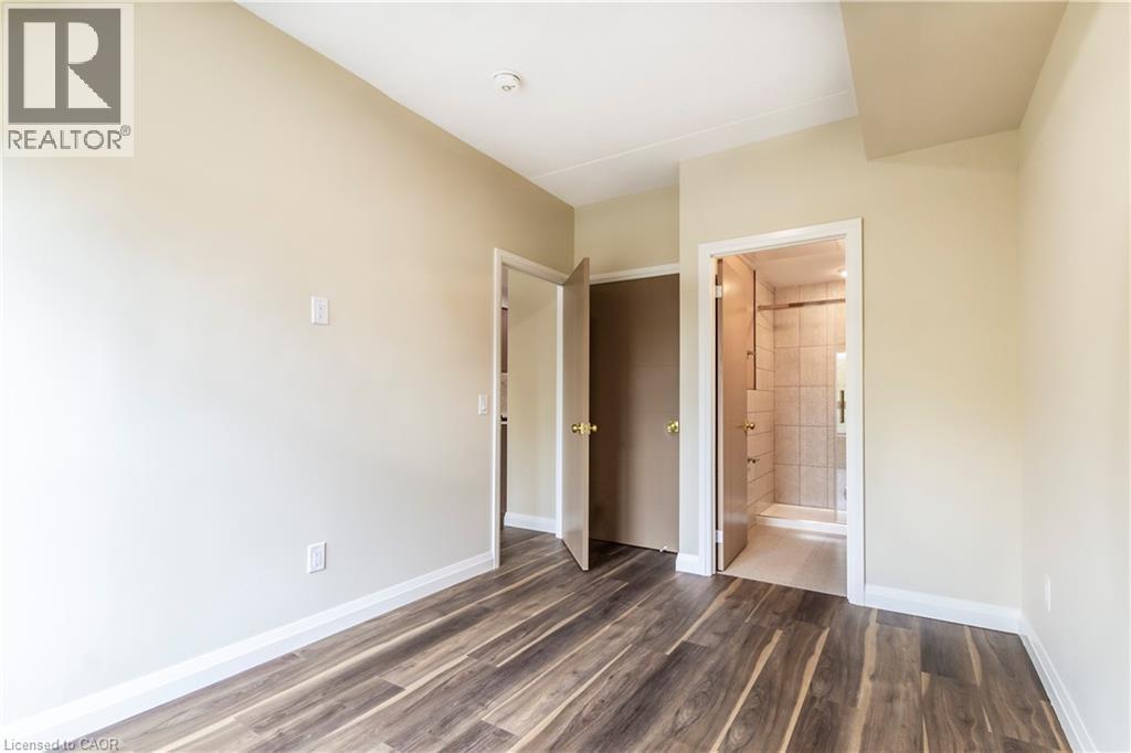 Unfurnished bedroom featuring dark wood-style flooring and connected bathroom - 580 Coldstream Drive Unit# 212, Waterloo, ON - Indoor Photo Showing Other Room