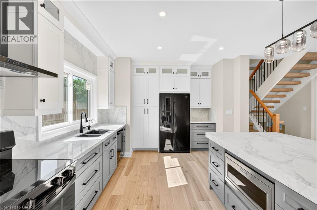Kitchen featuring gray cabinetry, light stone counters, pendant lighting, appliances with stainless steel finishes, and ventilation hood - 4006 Flemish Drive, Burlington, ON - Indoor Photo Showing Kitchen With Double Sink