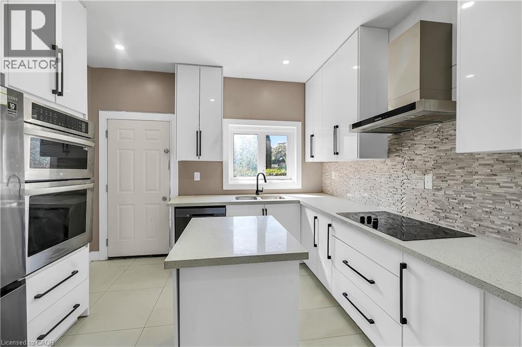 Kitchen with a kitchen island, white cabinets, wall chimney range hood, light stone countertops, and stainless steel appliances - 334 Cannon Street E, Hamilton, ON - Indoor Photo Showing Kitchen With Double Sink With Upgraded Kitchen