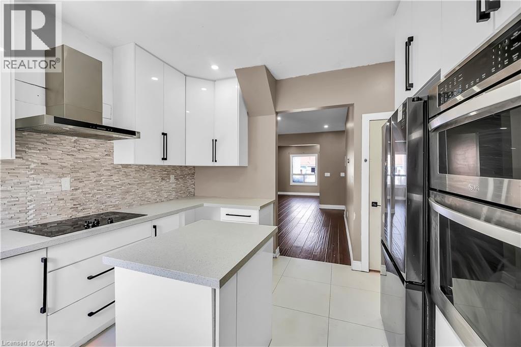 Kitchen featuring black appliances, white cabinets, wall chimney exhaust hood, light tile patterned flooring, and a kitchen island - 334 Cannon Street E, Hamilton, ON - Indoor Photo Showing Kitchen With Upgraded Kitchen