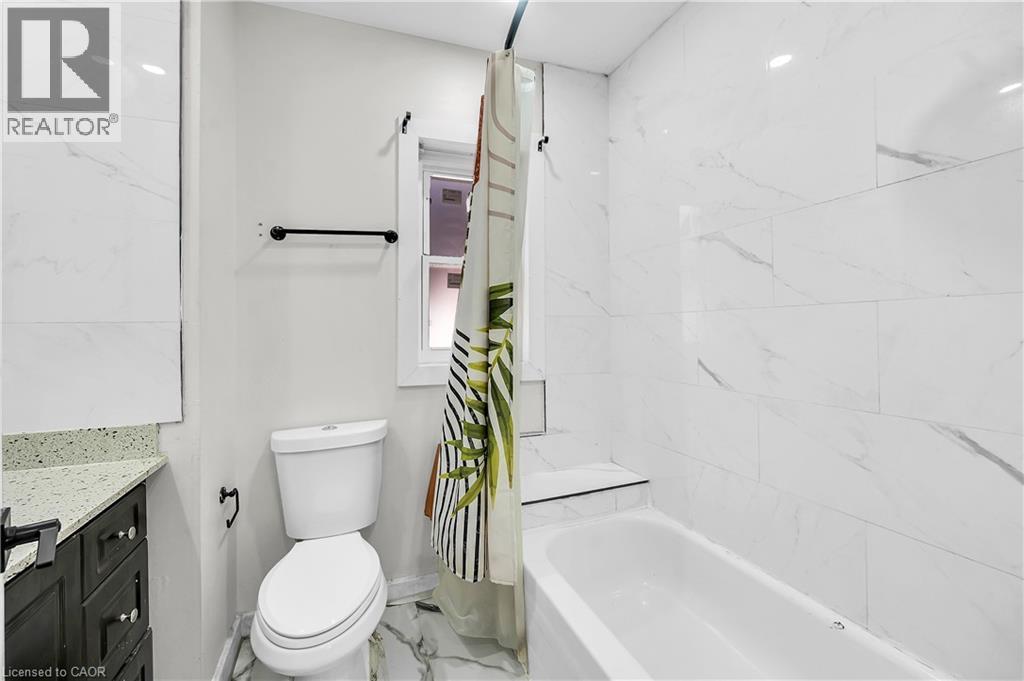 Bathroom featuring vanity, shower / bath combo, and marble look tile flooring - 334 Cannon Street E, Hamilton, ON - Indoor Photo Showing Bathroom
