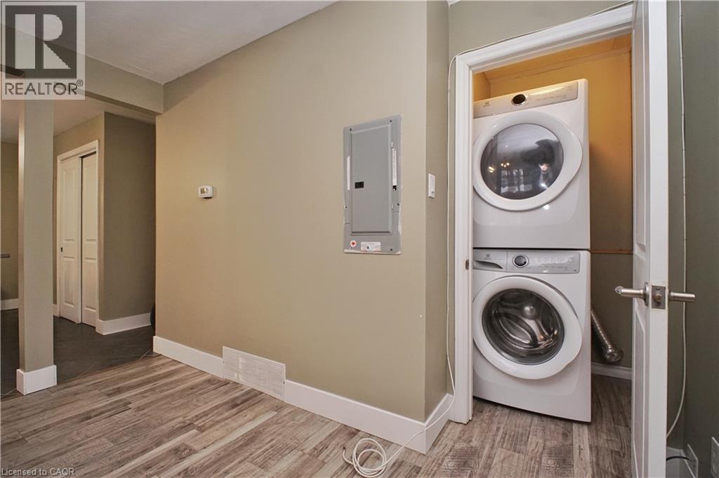 Laundry area featuring electric panel, estacked washer and dryer, and wood finished floors - 61 Bosworth Crescent, Kitchener, ON - Indoor Photo Showing Laundry Room
