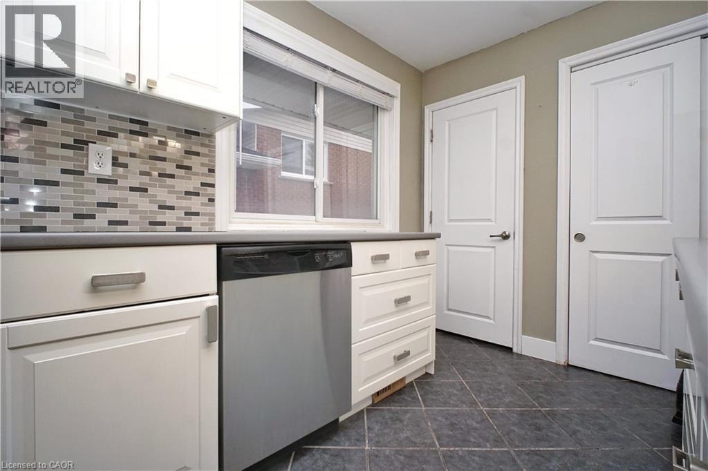 Kitchen with white cabinets, dishwasher, dark tile patterned floors, tasteful backsplash, and light countertops - 61 Bosworth Crescent, Kitchener, ON - Indoor