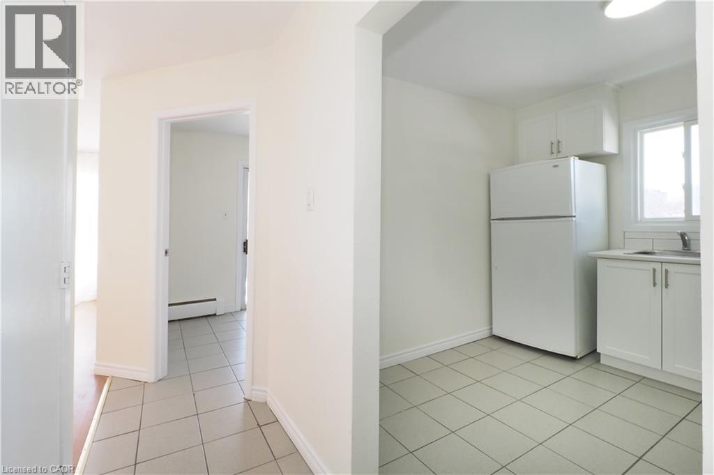 Kitchen with white cabinets, freestanding refrigerator, light countertops, a baseboard heating unit, and light tile patterned floors - 24 Austin Drive, Waterloo, ON - Indoor Photo Showing Kitchen