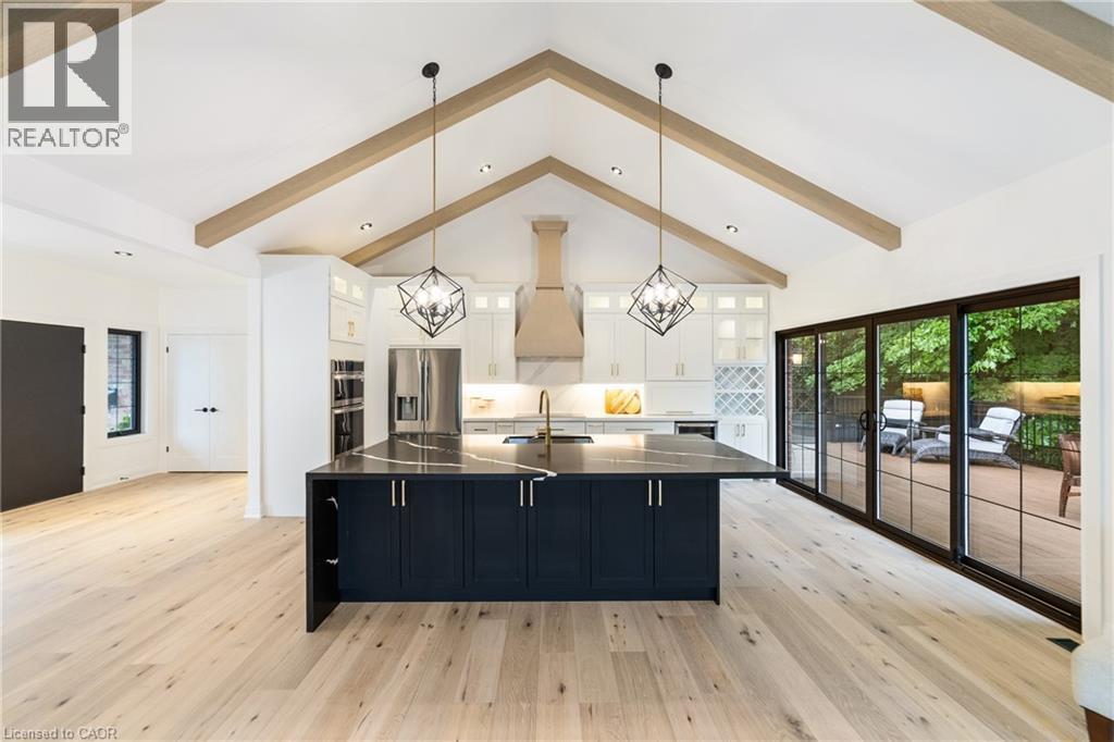 Kitchen with all new stainless steel appliances, custom white cabinetry with additional cabinets in island, induction stove top, luxury flooring, garden doors to the right, beam ceiling, display cabin - 515 Hamilton Drive, Ancaster, ON - Indoor Photo Showing Kitchen