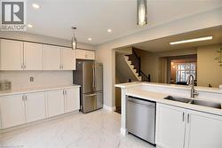 Kitchen with white cabinetry, appliances with stainless steel finishes, hanging light fixtures, light marble finish flooring, and backsplash -