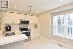 Kitchen featuring stainless steel appliances, white cabinets, pendant lighting, light marble finish flooring, and recessed lighting -