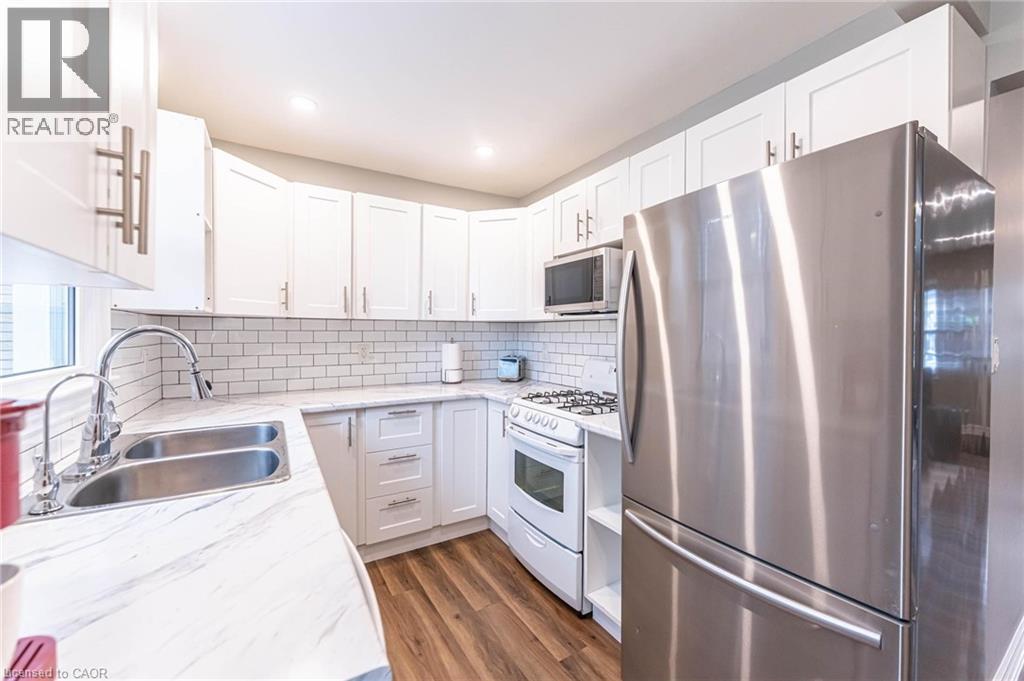 Kitchen featuring appliances with stainless steel finishes, white cabinetry, dark wood finished floors, tasteful backsplash, and light stone countertops - 140 Royal Avenue, Hamilton, ON - Indoor Photo Showing Kitchen With Double Sink With Upgraded Kitchen