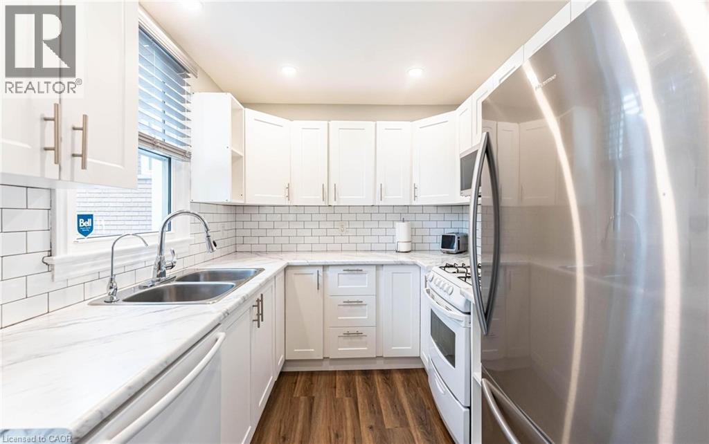 Kitchen featuring appliances with stainless steel finishes, white cabinetry, dark wood-type flooring, light stone counters, and decorative backsplash - 140 Royal Avenue, Hamilton, ON - Indoor Photo Showing Kitchen With Double Sink With Upgraded Kitchen