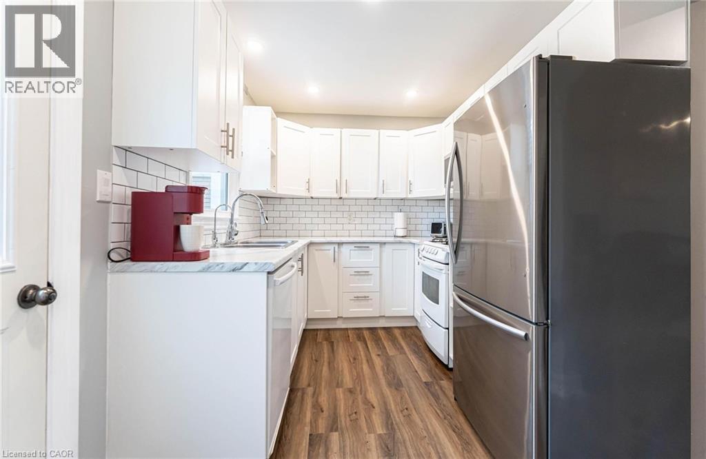 Kitchen with appliances with stainless steel finishes, white cabinetry, decorative backsplash, and dark wood-style floors - 140 Royal Avenue, Hamilton, ON - Indoor Photo Showing Kitchen With Upgraded Kitchen