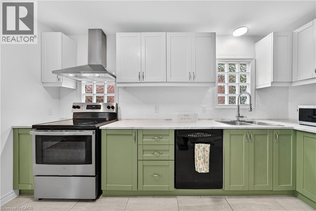Kitchen featuring green cabinetry, appliances with stainless steel finishes, white cabinetry, and wall chimney exhaust hood - 421 East 36Th Street, Hamilton, ON - Indoor Photo Showing Kitchen With Stainless Steel Kitchen With Double Sink