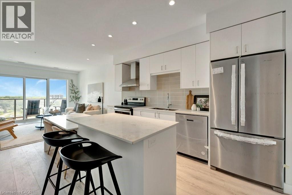 Kitchen featuring appliances with stainless steel finishes, wall chimney exhaust hood, a kitchen island, decorative backsplash, and light wood-style floors - 15 Glebe Street Unit# 1511, Cambridge, ON - Indoor Photo Showing Kitchen With Upgraded Kitchen