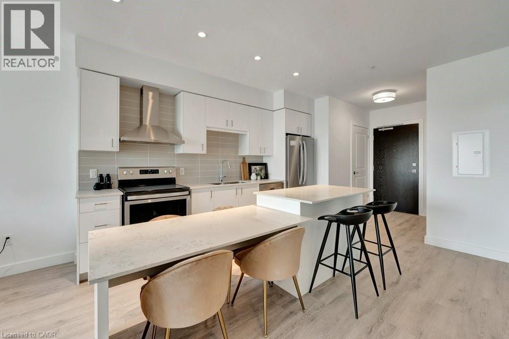 Kitchen with wall chimney range hood, stainless steel appliances, light wood finished floors, tasteful backsplash, and white cabinetry - 15 Glebe Street Unit# 1511, Cambridge, ON - Indoor Photo Showing Kitchen With Upgraded Kitchen