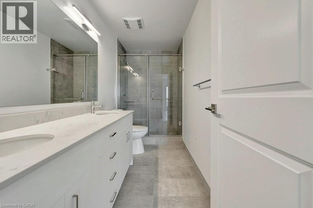 Full bathroom with double vanity, a stall shower, and tile patterned floors - 15 Glebe Street Unit# 1511, Cambridge, ON - Indoor Photo Showing Bathroom