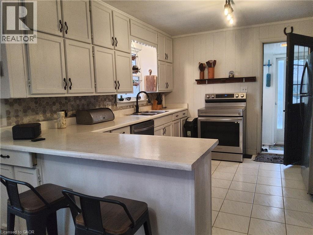 Kitchen featuring a peninsula, electric range, light countertops, a kitchen breakfast bar, and crown molding - 509 Queensway W, Simcoe, ON - Indoor Photo Showing Kitchen With Double Sink