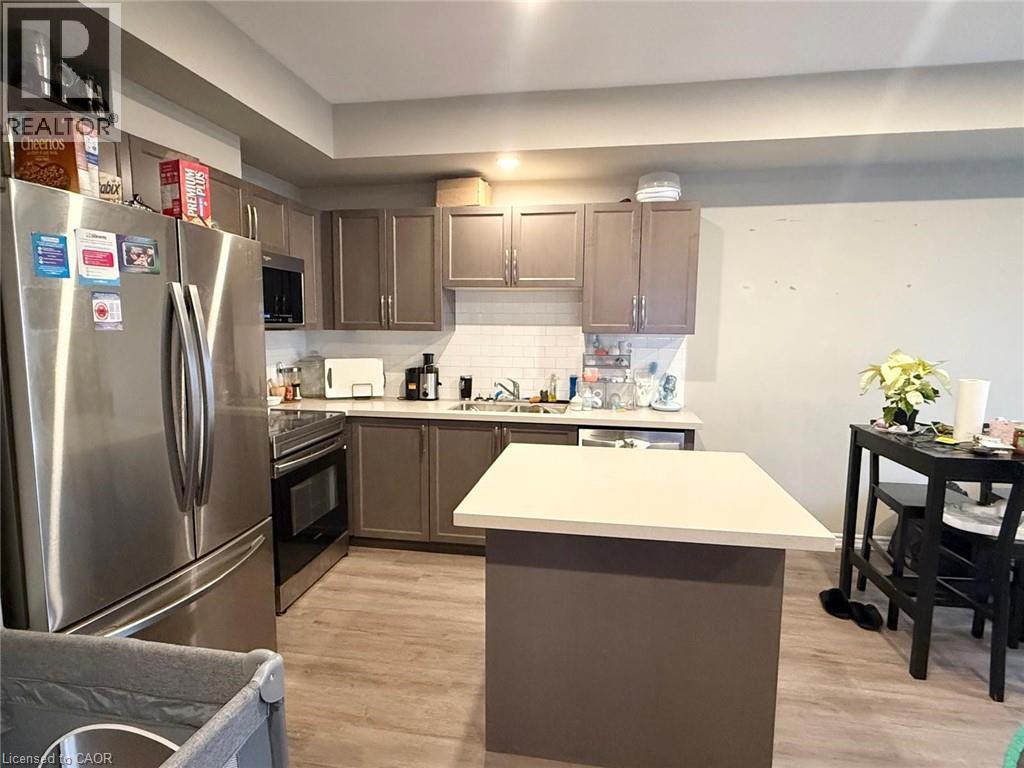 Kitchen with appliances with stainless steel finishes, a center island, light countertops, and light wood finished floors - 65 Old School Trail Unit# 36, Welland, ON - Indoor Photo Showing Kitchen