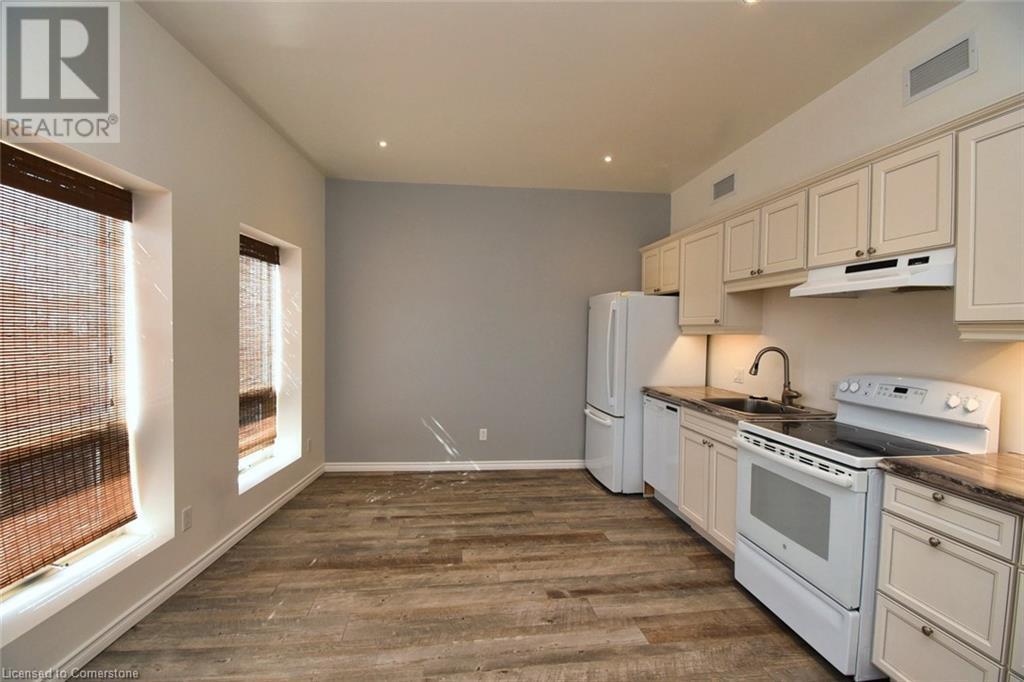 Kitchen featuring white appliances, visible vents, dark wood finished floors, a sink, and under cabinet range hood - 329 King Street E Unit# 3, Hamilton, ON - Indoor Photo Showing Kitchen