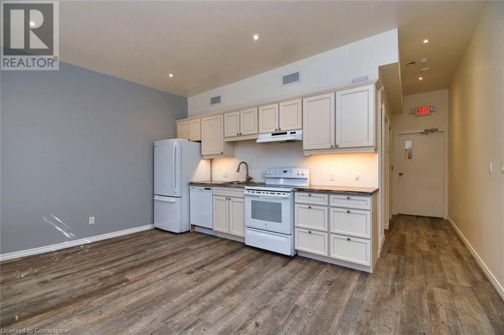 Kitchen with under cabinet range hood, visible vents, white appliances, and dark wood-style floors - 329 King Street E Unit# 3, Hamilton, ON - Indoor Photo Showing Kitchen