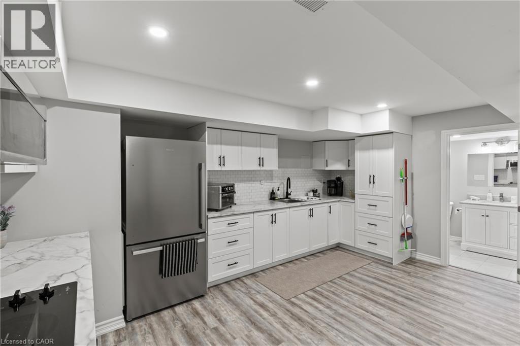 Kitchen with high quality fridge, white cabinetry, black electric stovetop, light wood finished floors, and backsplash - 62 Esther Crescent Unit# Lower, Thorold, ON - Indoor Photo Showing Kitchen