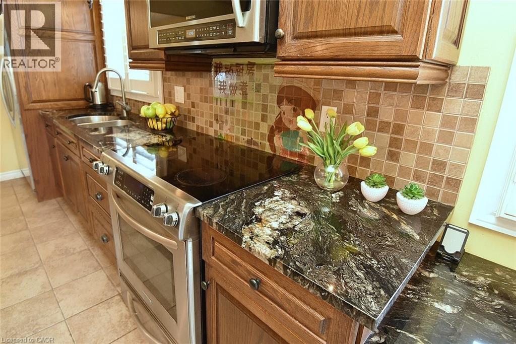 Kitchen with stainless steel appliances, brown cabinetry, light tile patterned floors, and backsplash - 43 Niska Drive, Waterdown, ON - Indoor Photo Showing Kitchen With Double Sink