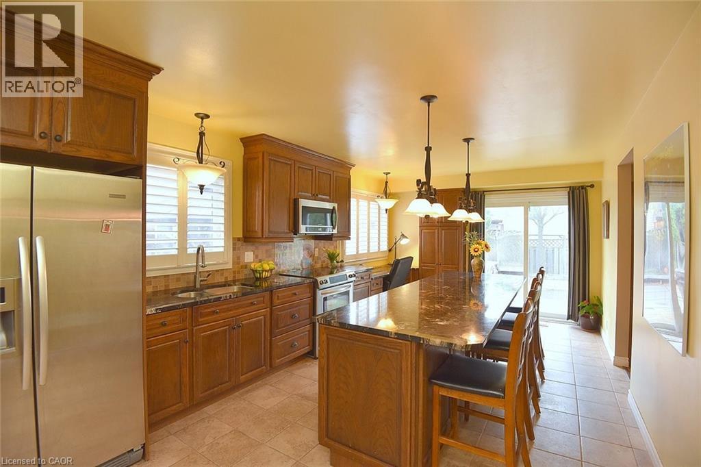 Kitchen featuring appliances with stainless steel finishes, brown cabinets, a breakfast bar area, dark stone countertops, and backsplash - 43 Niska Drive, Waterdown, ON - Indoor Photo Showing Kitchen With Upgraded Kitchen