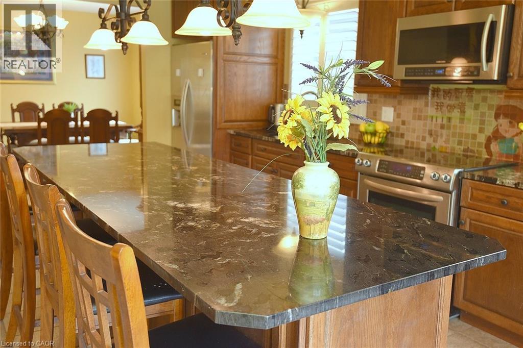 Kitchen with a breakfast bar, dark stone counters, stainless steel appliances, a large island, and hanging light fixtures - 43 Niska Drive, Waterdown, ON - Indoor Photo Showing Dining Room
