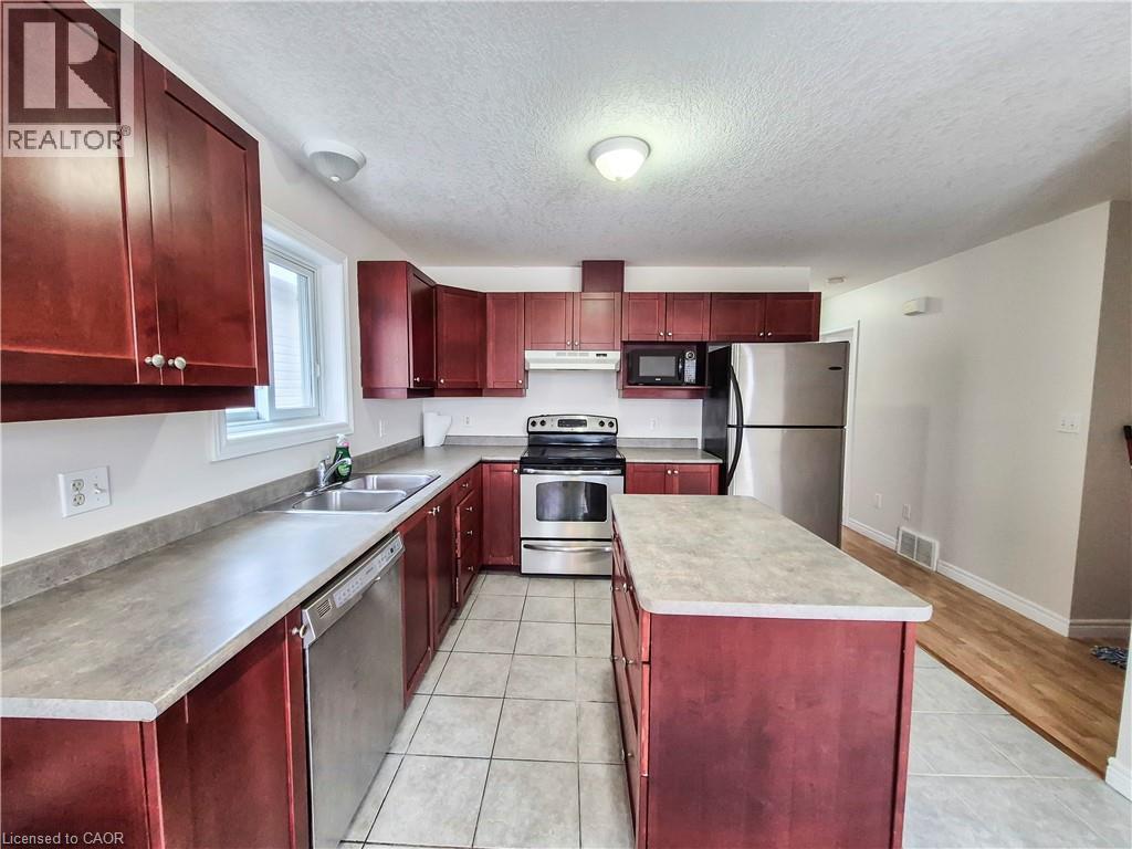 Kitchen with reddish brown cabinets, stainless steel appliances, a textured ceiling, a kitchen island, and light tile patterned floors - 132 Udvari Crescent Unit# 3, Kitchener, ON - Indoor Photo Showing Kitchen With Double Sink