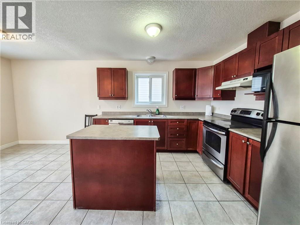 Kitchen with reddish brown cabinets, stainless steel appliances, a textured ceiling, a kitchen island, and under cabinet range hood - 132 Udvari Crescent Unit# 3, Kitchener, ON - Indoor Photo Showing Kitchen With Double Sink