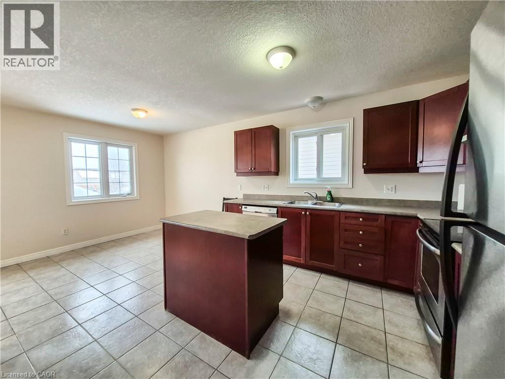 Kitchen featuring dark brown cabinets, a center island, stainless steel appliances, a textured ceiling, and light tile patterned floors - 132 Udvari Crescent Unit# 3, Kitchener, ON - Indoor Photo Showing Kitchen With Double Sink