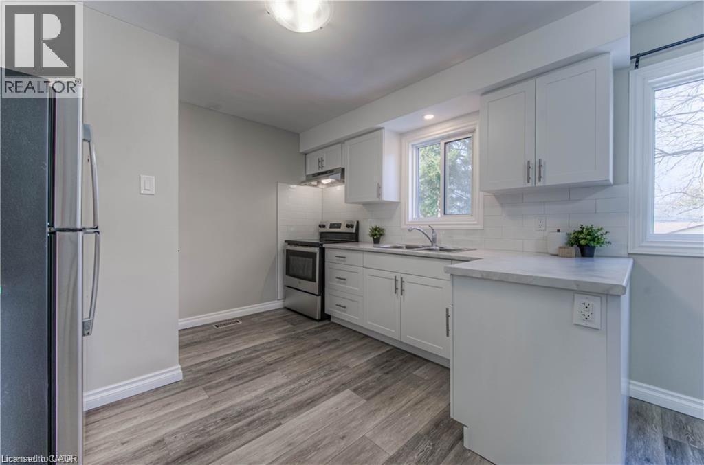 Kitchen with appliances with stainless steel finishes, white cabinets, decorative backsplash, and light wood-style flooring - 156 Donald Street, Kitchener, ON - Indoor Photo Showing Kitchen With Double Sink