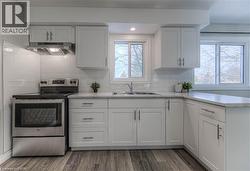 Kitchen with stainless steel electric range oven, under cabinet range hood, white cabinets, a peninsula, and dark wood finished floors -