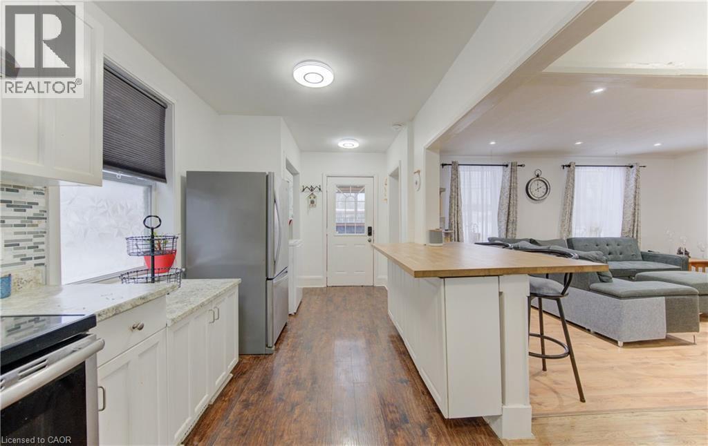 Kitchen featuring open floor plan, a breakfast bar area, appliances with stainless steel finishes, white cabinets, and dark wood-style floors - 569 Stirling Avenue S, Kitchener, ON - Indoor Photo Showing Kitchen