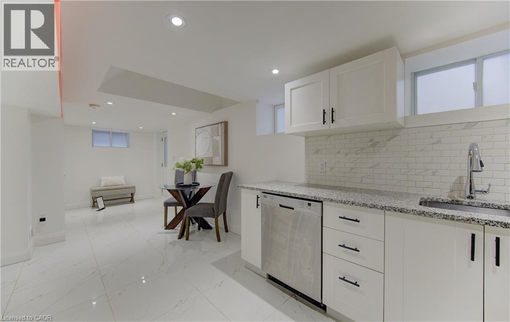 Kitchen featuring white cabinets, light stone counters, stainless steel dishwasher, decorative backsplash, and open floor plan - 569 Stirling Avenue S, Kitchener, ON - Indoor Photo Showing Kitchen With Upgraded Kitchen