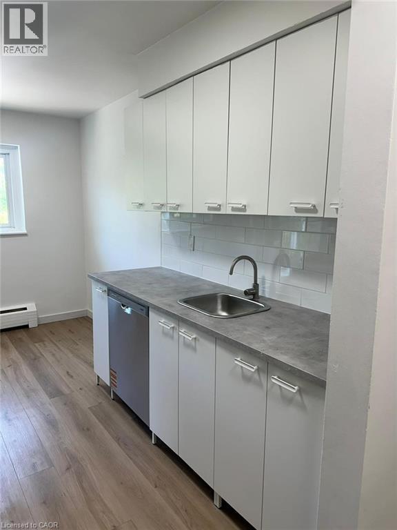 Kitchen with tasteful backsplash, baseboard heating, dishwasher, light wood-type flooring, and white cabinets - 145 Macgregor Crescent Unit# 1, Waterloo, ON - Indoor Photo Showing Kitchen