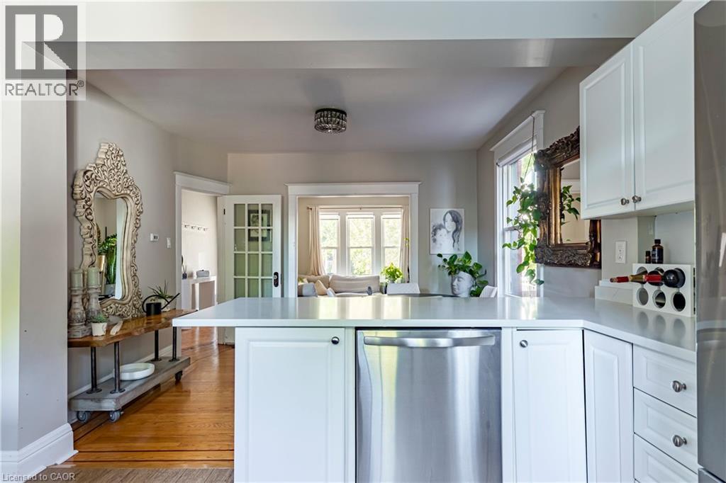 Kitchen featuring white cabinets, a peninsula, stainless steel appliances, light wood finished floors, and light countertops - 58 Chatham Street, Hamilton, ON - Indoor Photo Showing Kitchen