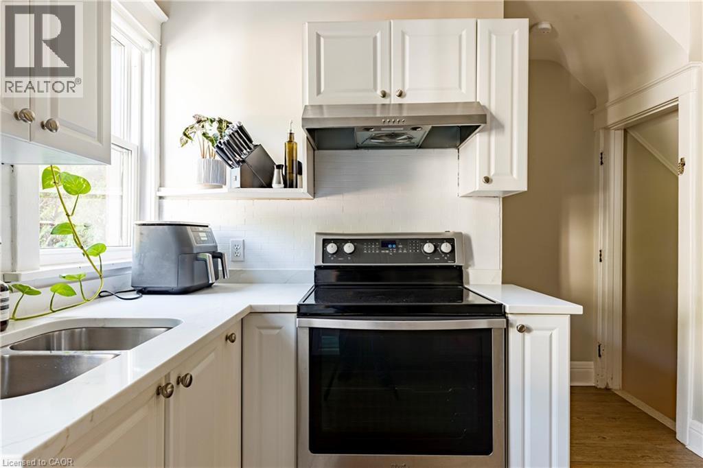 Kitchen featuring stainless steel electric range, tasteful backsplash, white cabinetry, and under cabinet range hood - 58 Chatham Street, Hamilton, ON - Indoor Photo Showing Kitchen With Double Sink