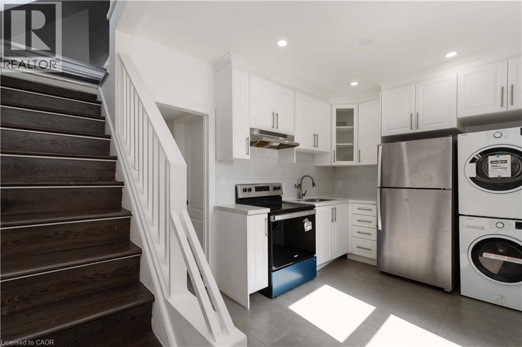 Kitchen featuring appliances with stainless steel finishes, light countertops, white cabinets, glass insert cabinets, and under cabinet range hood - 934 Barton Street E Unit# 2, Hamilton, ON - Indoor Photo Showing Laundry Room