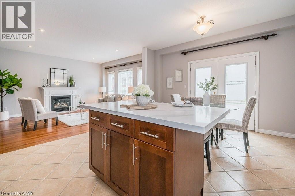 Kitchen featuring a kitchen island, a glass covered fireplace, open floor plan, light tile patterned flooring, and a kitchen bar - 609 Woolgrass Avenue, Waterloo, ON - Indoor With Fireplace