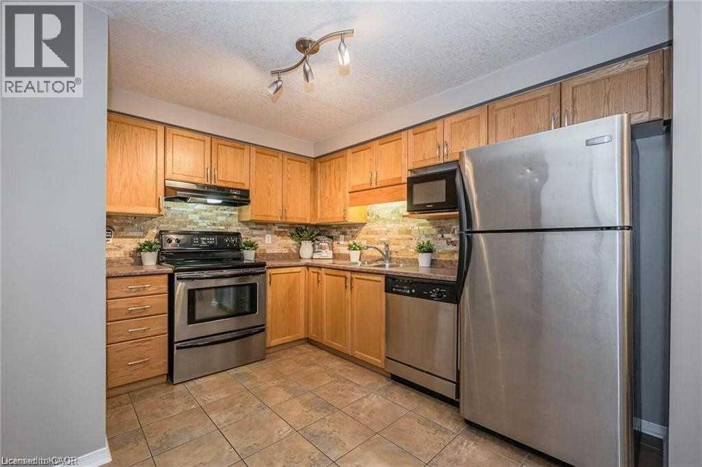 Kitchen featuring appliances with stainless steel finishes, a textured ceiling, under cabinet range hood, tasteful backsplash, and light stone countertops - 27 Max Becker Drive, Kitchener, ON - Indoor Photo Showing Kitchen