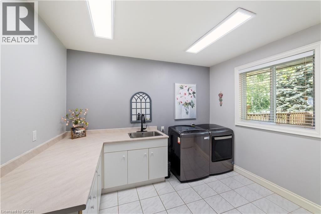 Laundry room on the main floor, large window, cabinets for extra storage, neutral ceramic tiles, extra LED lighting, sink, intercom. Not show is a large closet opposite the appliances. - 7775 St. Augustine Crescent, Niagara Falls, ON - Indoor Photo Showing Other Room