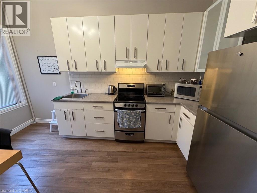 Kitchen with appliances with stainless steel finishes, white cabinets, dark wood-style floors, and tasteful backsplash - 175 John Street S, Hamilton, ON