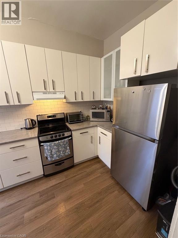 Kitchen featuring fridge, white cabinets, stove, glass insert cabinets, and dark wood-type flooring - 175 John Street S, Hamilton, ON